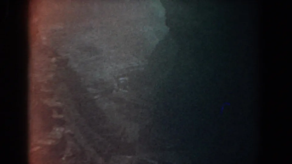 Low-light 1958 Yorktown 8mm frame of mottled rock, amber tinting, and a shadowed edge.