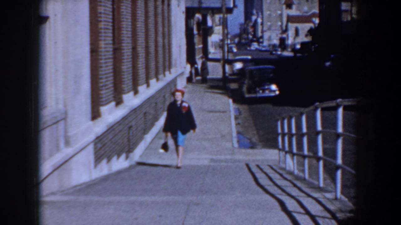 Woman in a red hat walks up a steep sidewalk beside a masonry building.