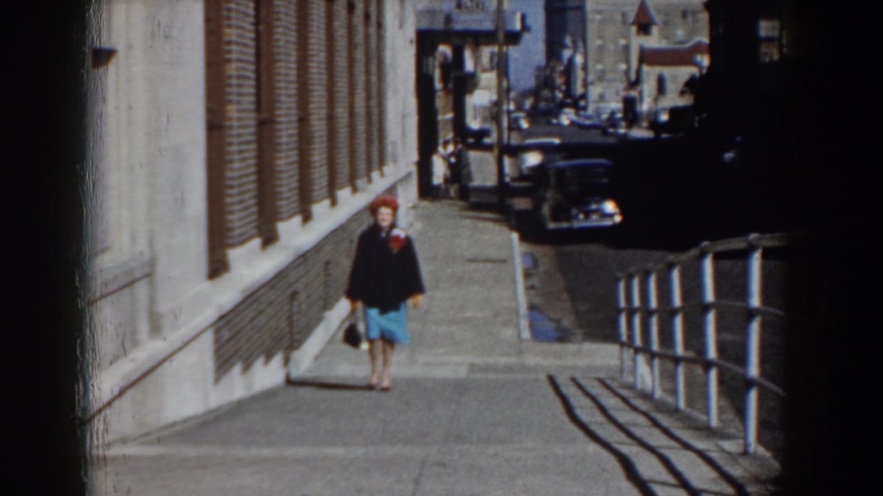 Woman approaches along the sidewalk with parked cars visible down the street.