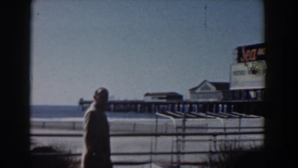 1958 Yorktown boardwalk view with a suited man passing railings near a pier and a large Sea and Ski advertisement.