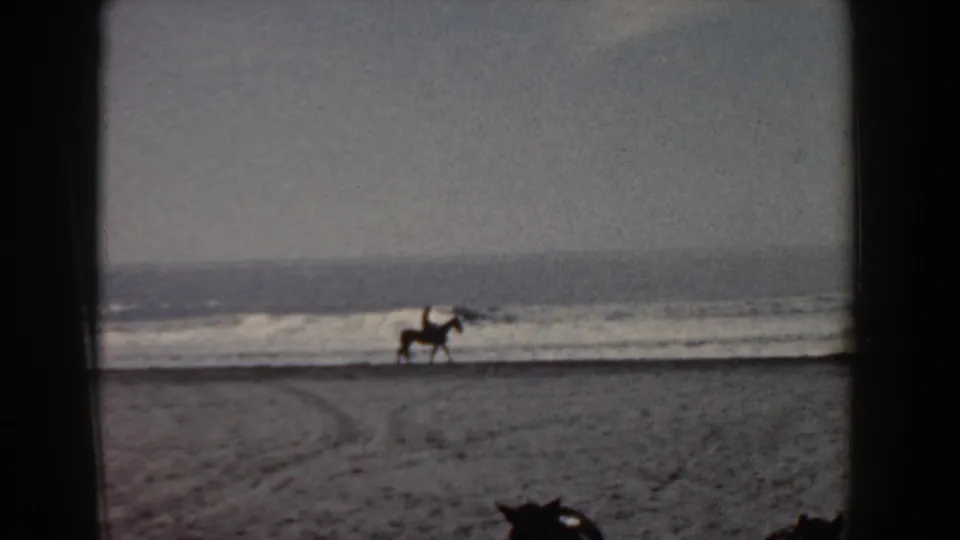 Distant horseback rider on a Yorktown beach in 1958, silhouetted against low waves and a hazy ocean horizon.
