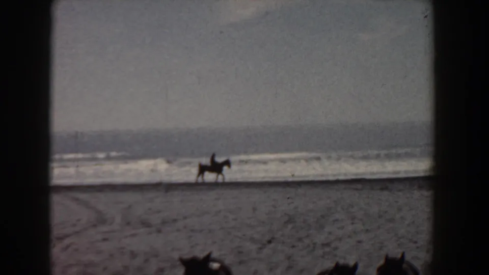 1958 Yorktown home-movie frame showing a horse and rider silhouetted along the shoreline under an overcast sky.