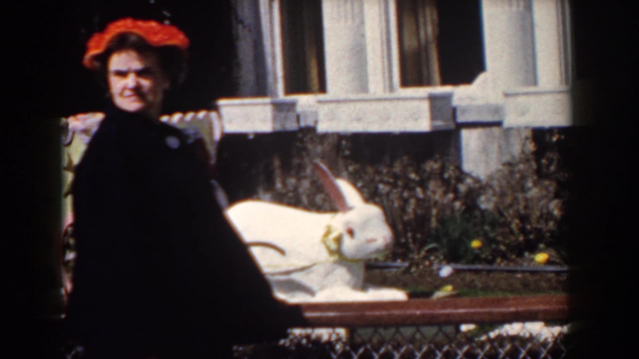 In Yorktown, Virginia, 1958, a woman in a red hat and dark coat stands near a large white rabbit statue in a sunny garden.