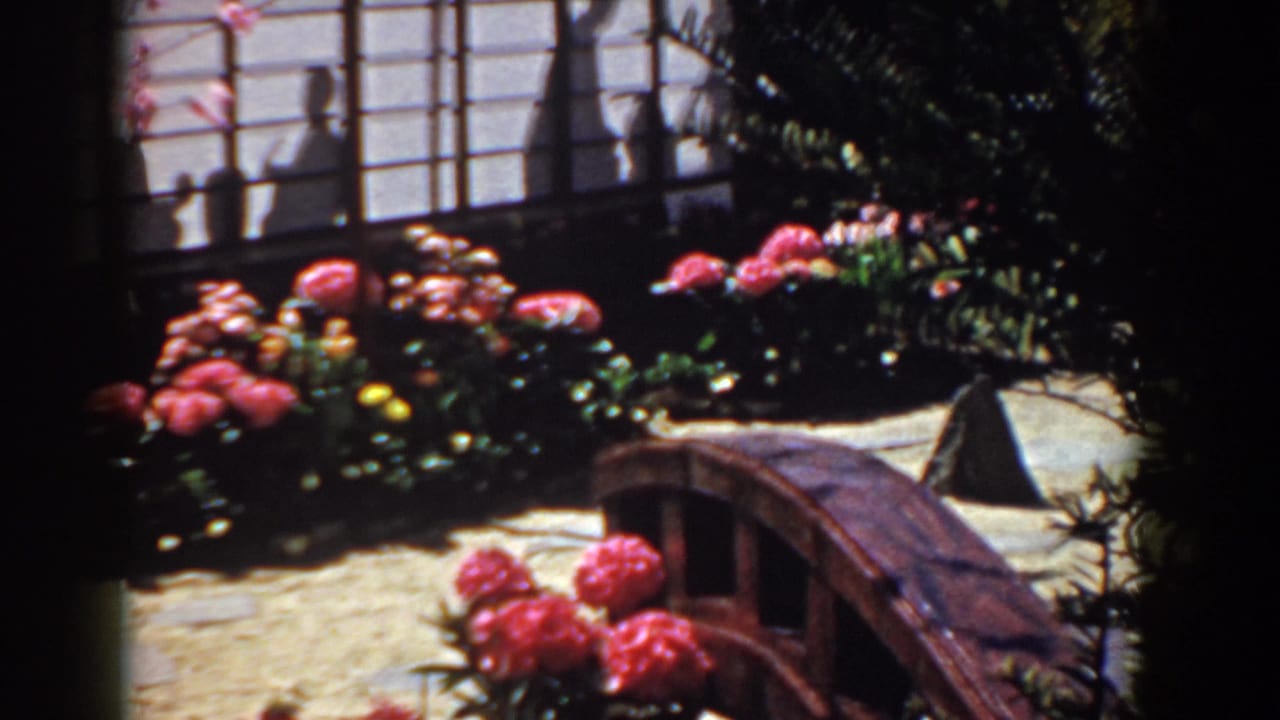 1958 Yorktown garden display with pink blossoms, dense foliage, shoji-style screens, figure shadows, and an arched wooden bridge.