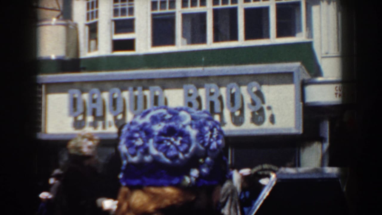 Pedestrians in period clothing pass a DAQUIN BROS. storefront sign in 1958 Yorktown, Virginia street footage.