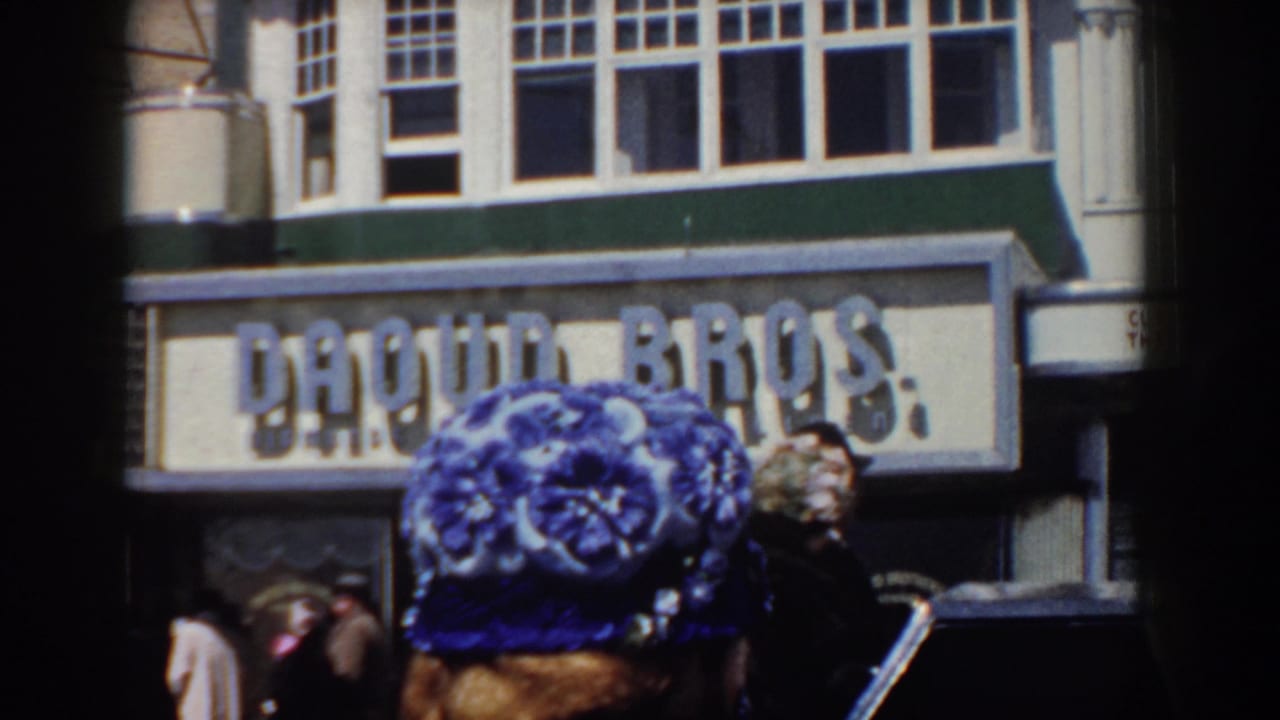 A woman or passerby wearing a blue floral hat stands near the DAQUIN BROS. sign in the Yorktown street scene.