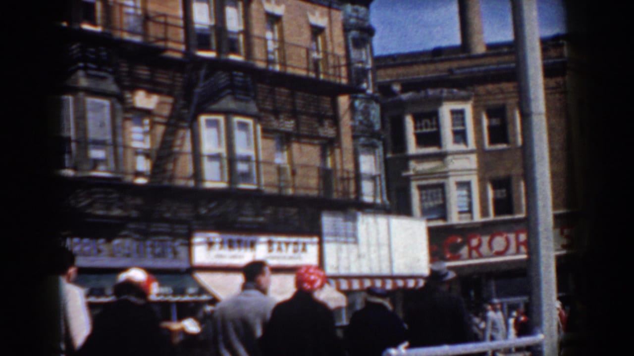 1958 Yorktown parade spectators face brick storefronts and painted signs along a sunlit commercial street.