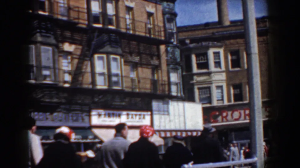 1958 Yorktown parade spectators face brick storefronts and painted signs along a sunlit commercial street.