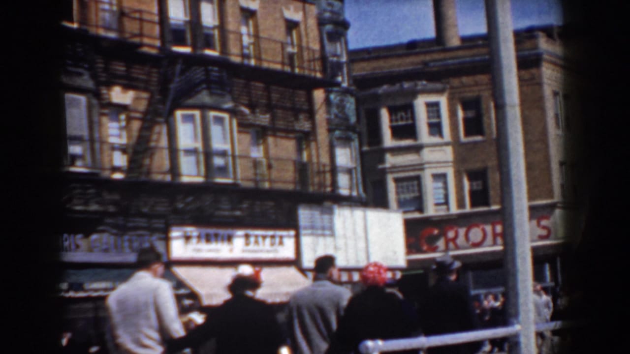 Spectators in coats and hats stand near a parade barrier on a Yorktown commercial street in 1958.