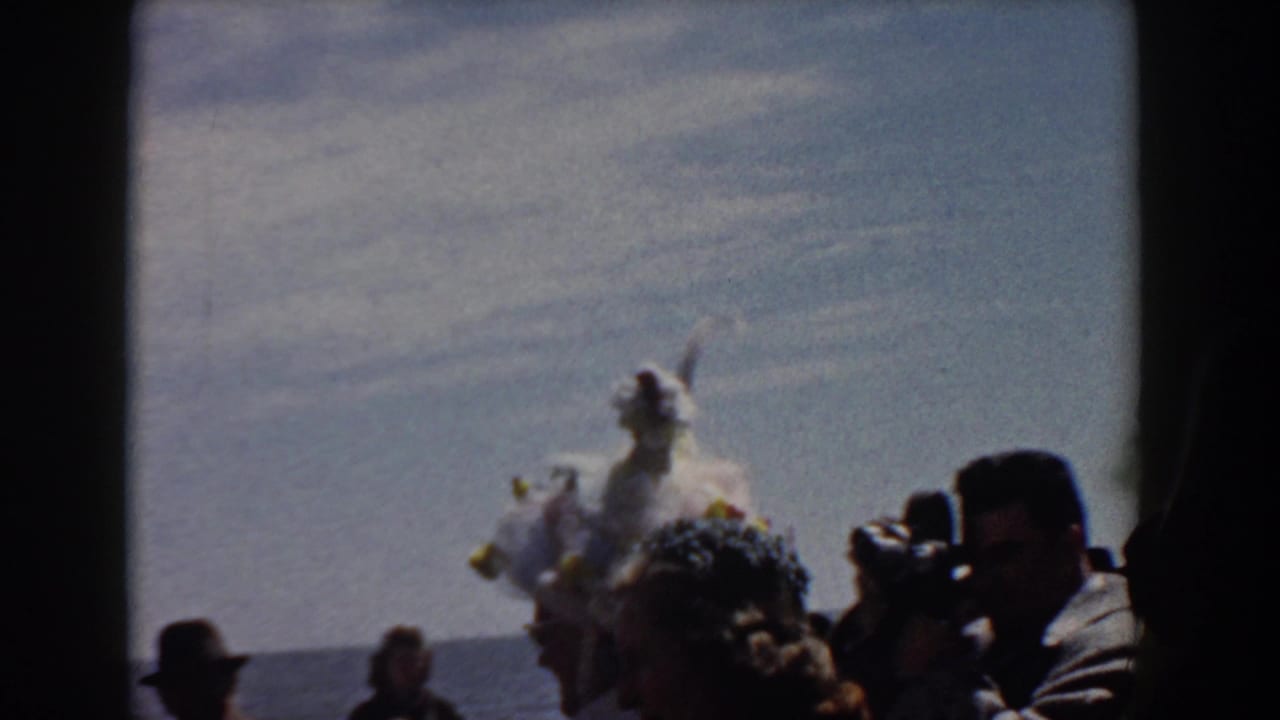 A feathered white costume appears among Yorktown spectators, with a photographer-like figure and water in the background.