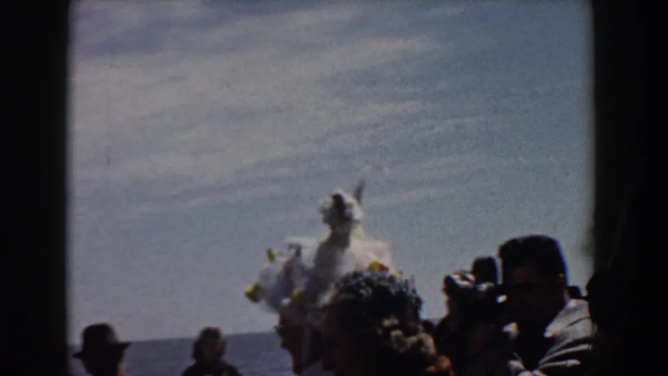 A feathered white costume appears among Yorktown spectators, with a photographer-like figure and water in the background.
