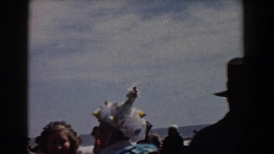 A Yorktown crowd watches a feathered white costume near the waterfront, with faces partly shadowed by the 8mm exposure.