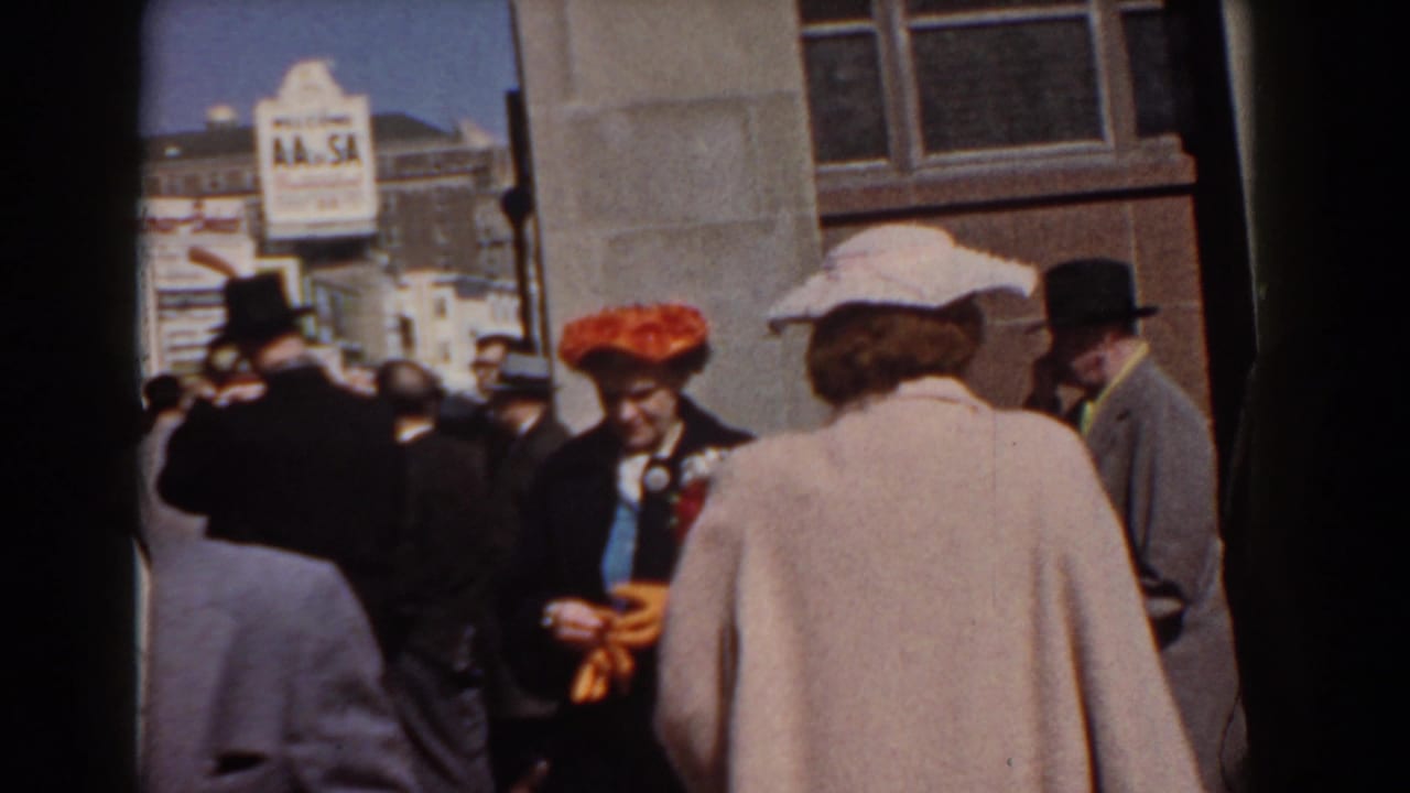 1958 Yorktown street view with a woman in a red hat and orange gloves standing among men and women in coats and hats.