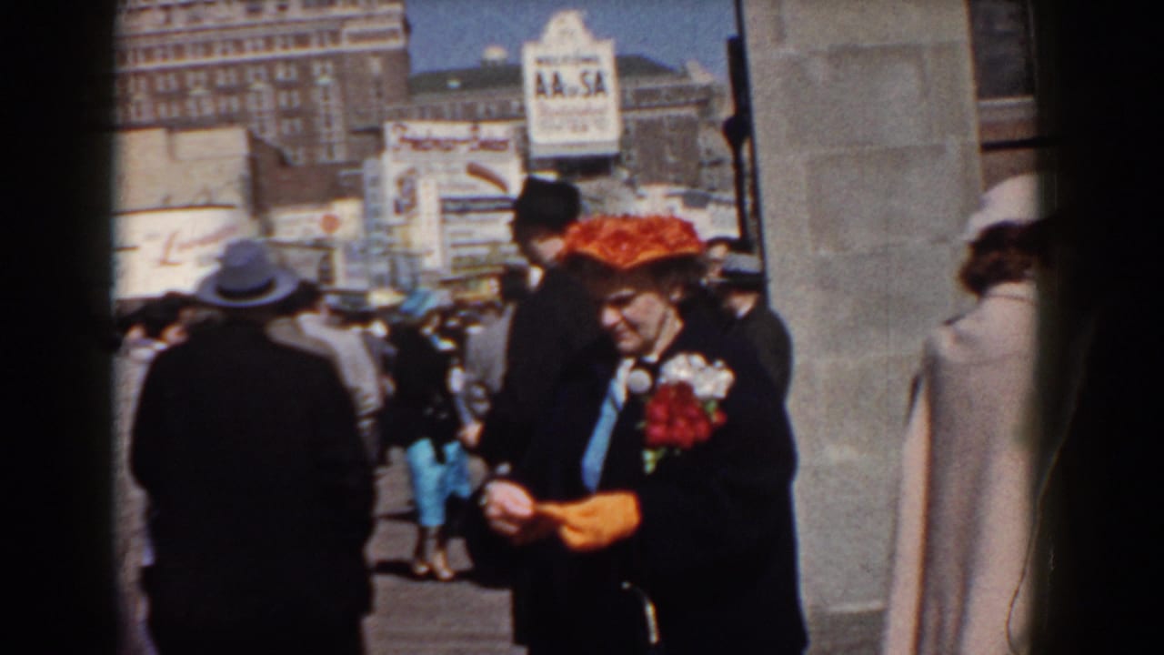 Woman in red hat looks down while adjusting orange gloves in a crowd.