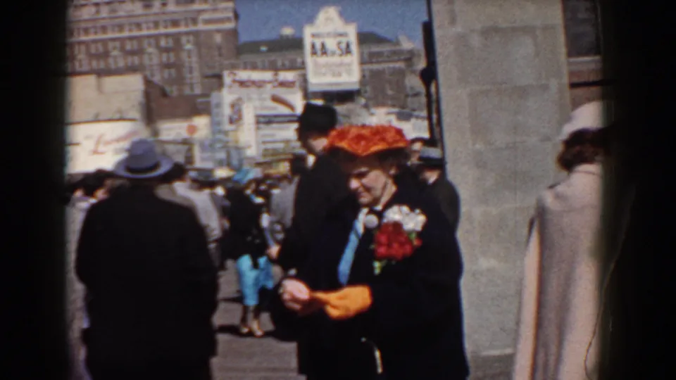 The woman in a red hat and dark coat adjusts her orange gloves while standing among pedestrians in Yorktown, Virginia, in 1958.