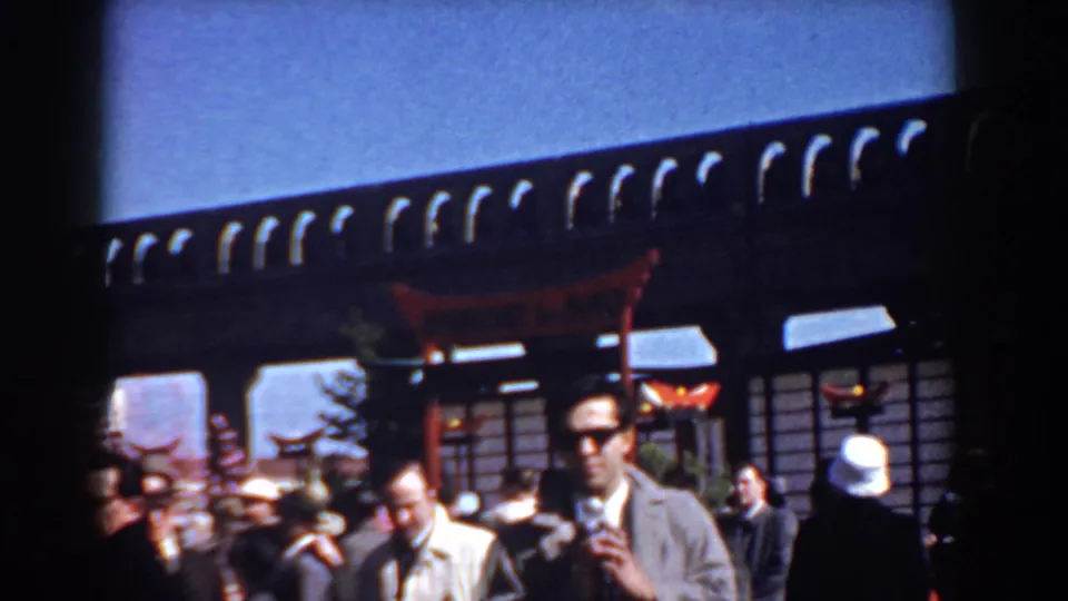 At the 1958 Yorktown gathering, a tall man in glasses stands near other visitors beneath a Japanese-style torii and dark wooden facade.