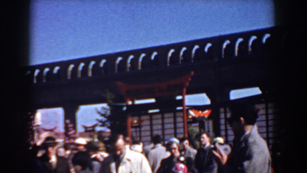 1958 Yorktown home-movie frame showing people near a dark-roofed storefront or pavilion with red posts and awnings.