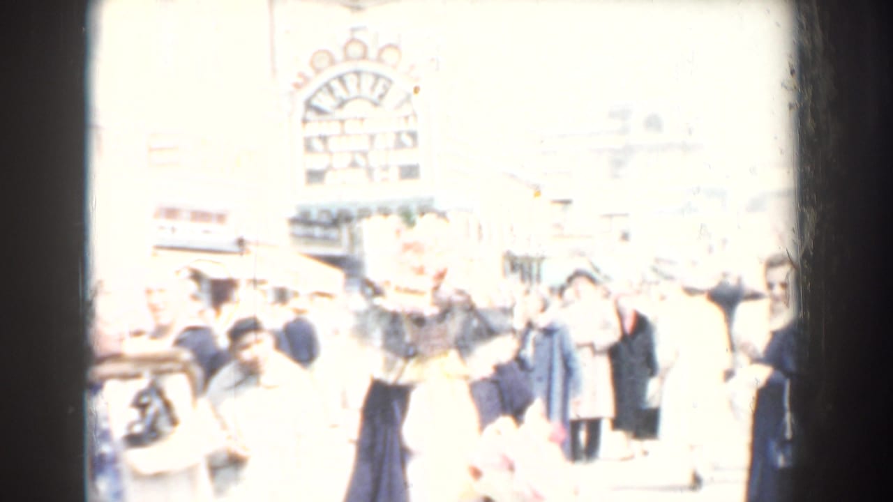 Overexposed 1958 Yorktown street frame with pedestrians passing shops and a prominent theater-style sign in the background.
