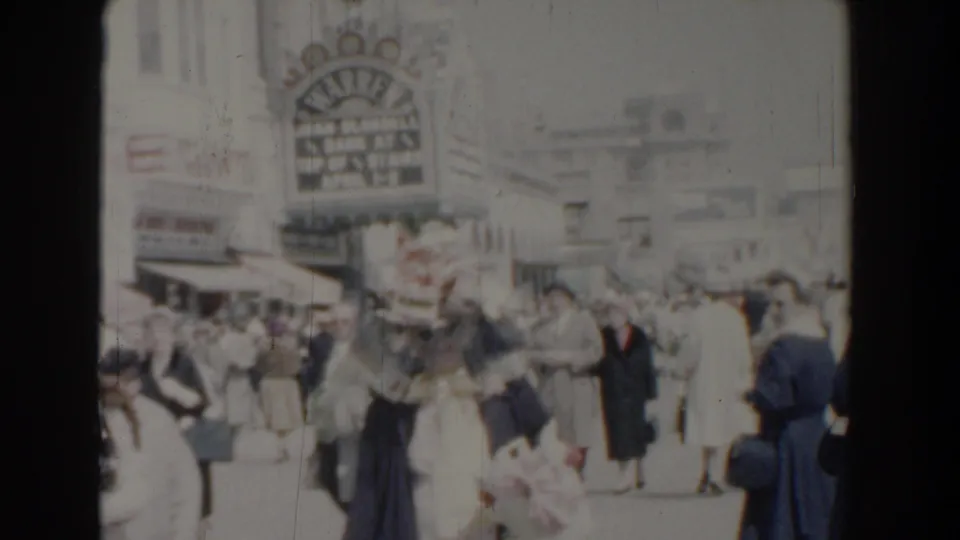 Soft 1958 Yorktown street frame showing a crowd near shop awnings and a prominent sign above the storefronts.