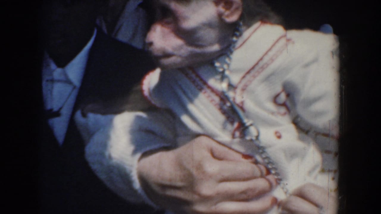 1958 Yorktown beach home movie frame showing a small monkey in a white outfit with red trim and a chain collar being held close.