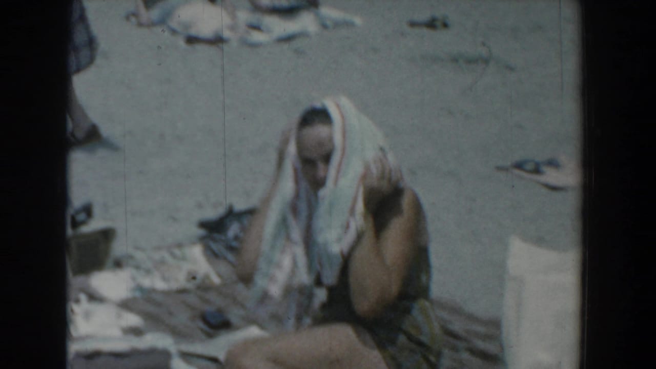 Woman seated on a beach towel drying her hair with a striped towel.