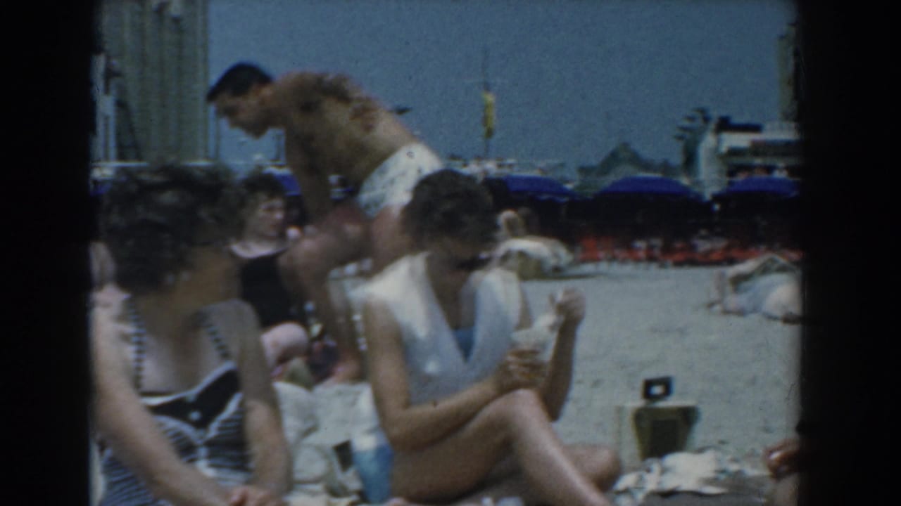The Yorktown beach footage shows a small group of adults on the sand, including seated women and a shirtless man standing near umbrellas and buildings.
