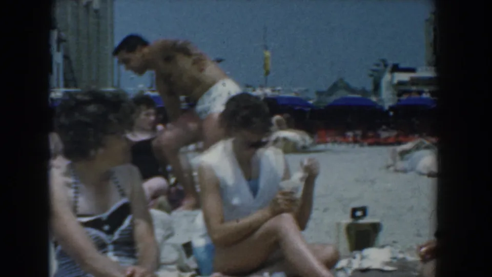 The Yorktown beach footage shows a small group of adults on the sand, including seated women and a shirtless man standing near umbrellas and buildings.