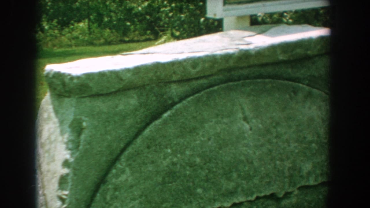 Weathered stone monument partly framed by dark film edges and greenery.