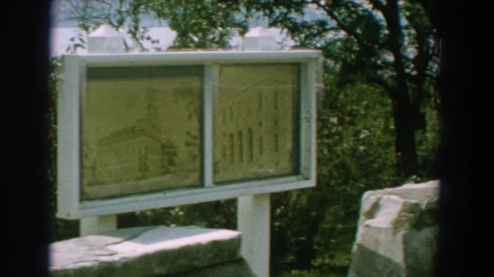 Florida 1959 8mm frame centered on a white-framed sign with two sepia building drawings beside trees and stonework.
