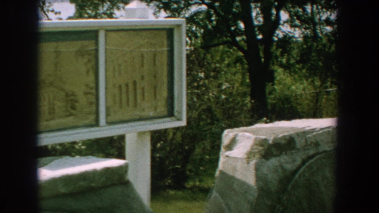 Framed historical sign panels beside grey stonework and trees.