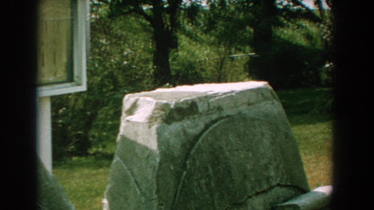 Grey stone monument and sign panel framed by trees and lawn.