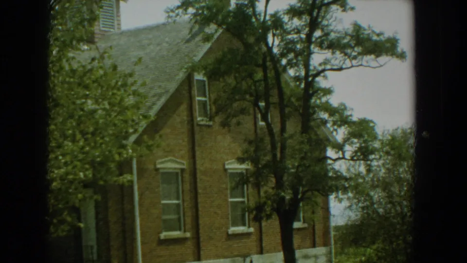 1959 Florida 8mm frame showing a brick residential exterior with white-trimmed windows, mature trees, and a gabled roof.