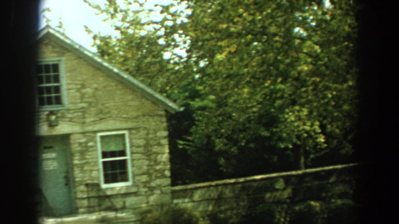 Small tan stone building with green door and trees behind it.
