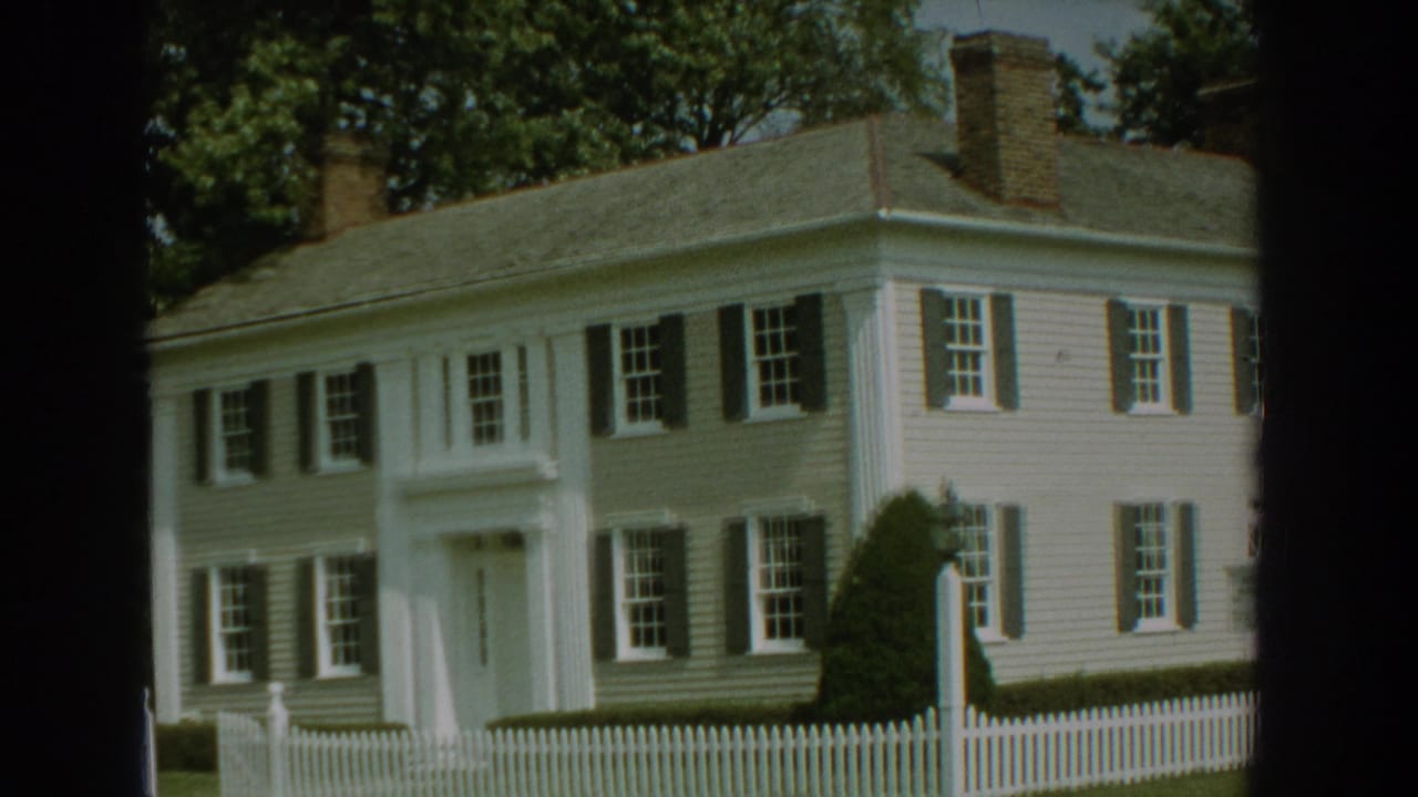 Colonial-style house facade with shutters, columns and a marker sign.