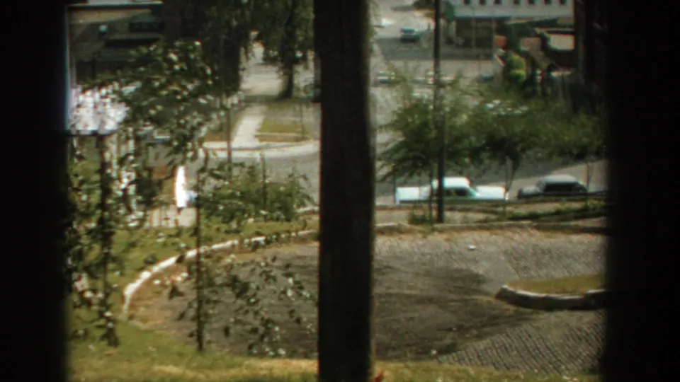 1959 Florida residential street scene from an upper window, with a curved paved road, young trees, sidewalks, and light-colored cars.