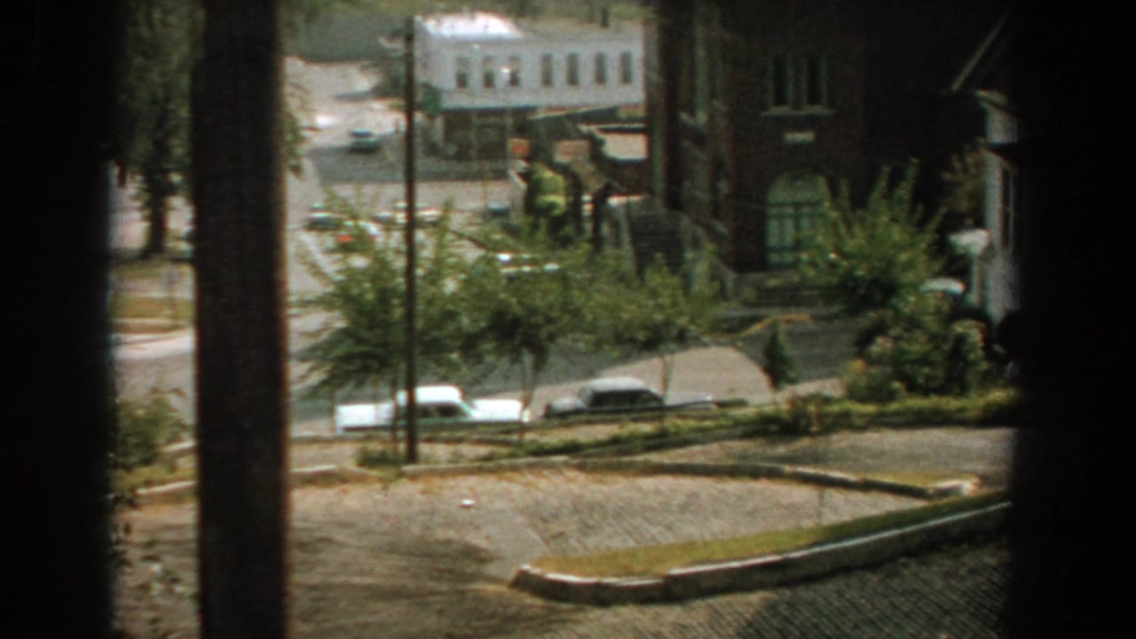 Elevated street view with parked cars, trees, brick buildings, and dark foreground posts.