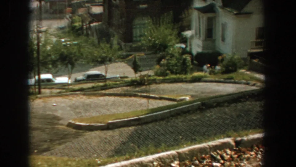 Elevated 1959 Florida neighborhood view showing a curved paved street, parked cars, houses, trees, and a foreground post.