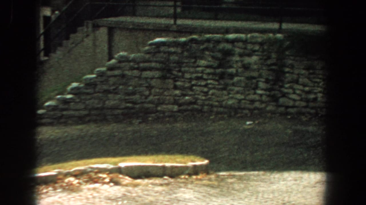 Curving stone wall beside a path, with stairs and railings in the background.
