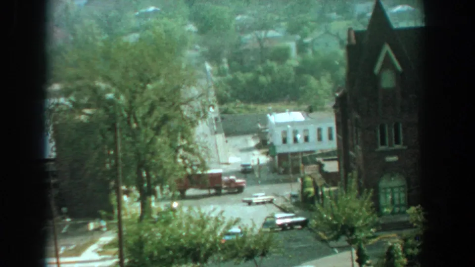 1959 Florida 8mm frame showing an elevated view of cars and a truck near a tree-lined intersection and church-like brick building.
