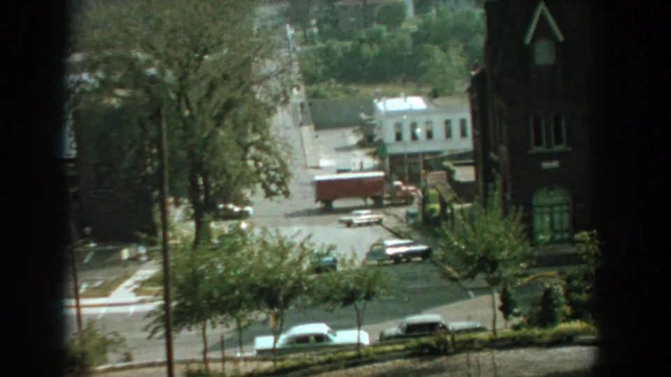 1959 Florida street view from above, with a truck and sedans passing near trees, sidewalks, and a church-like building.