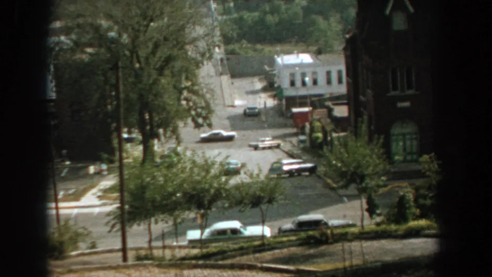 1959 Florida 8mm frame of a red-toned truck and period cars moving through a sunlit intersection from an elevated viewpoint.