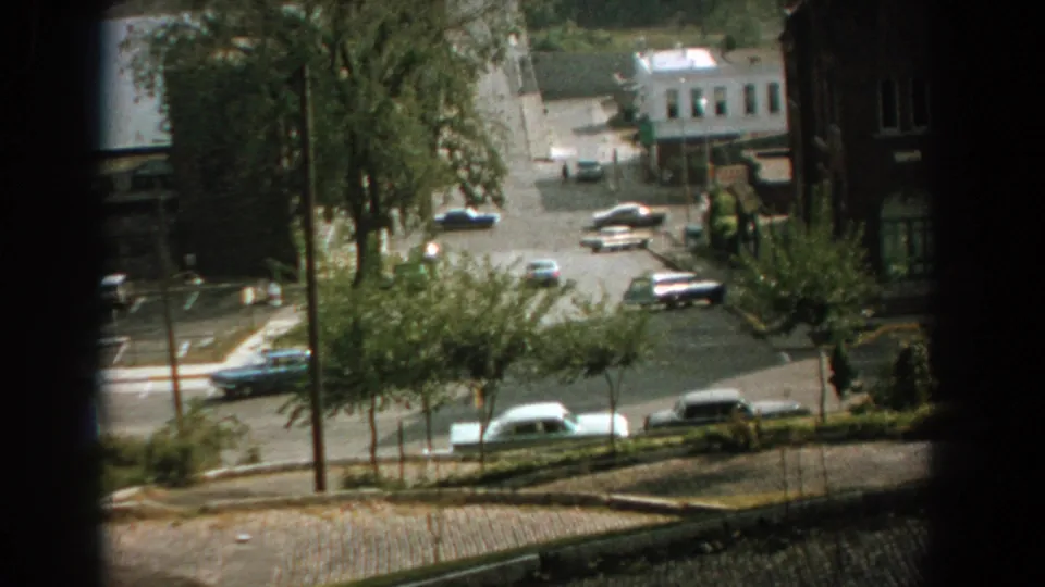 1959 Florida elevated street frame showing period cars near a leafy intersection and church-like brick building in soft 8mm color.