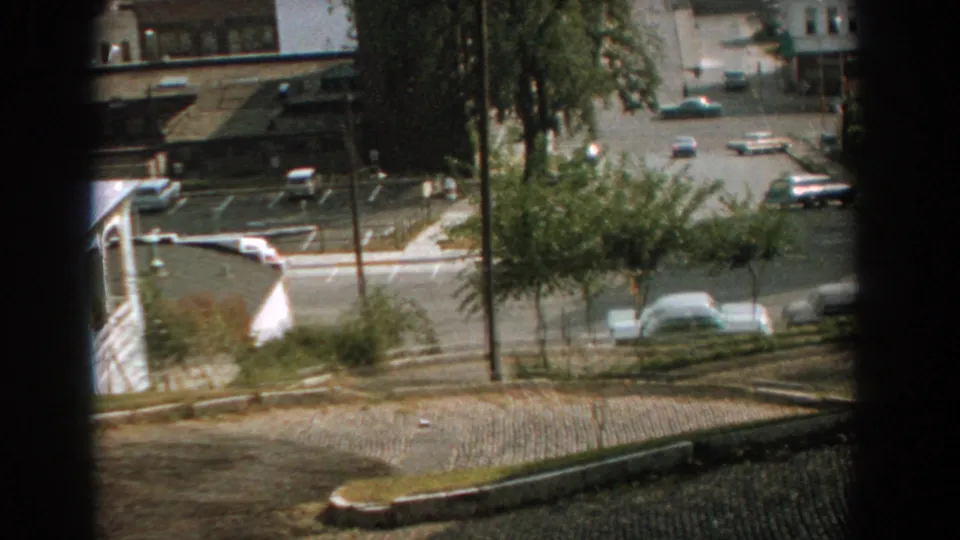 Late-1950s Florida street corner with light car traffic, low-rise buildings, trees, and a dark window edge in the frame.