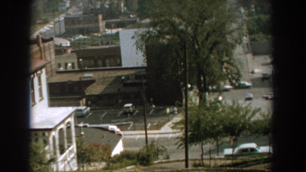 Overhead view of a street corner, parked cars, trees, and low buildings.