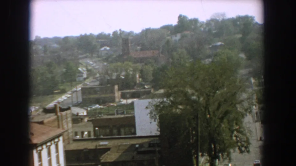 1959 Florida 8mm view over a quiet street district, with trees, low rooftops, distant houses, and a dark foreground border.
