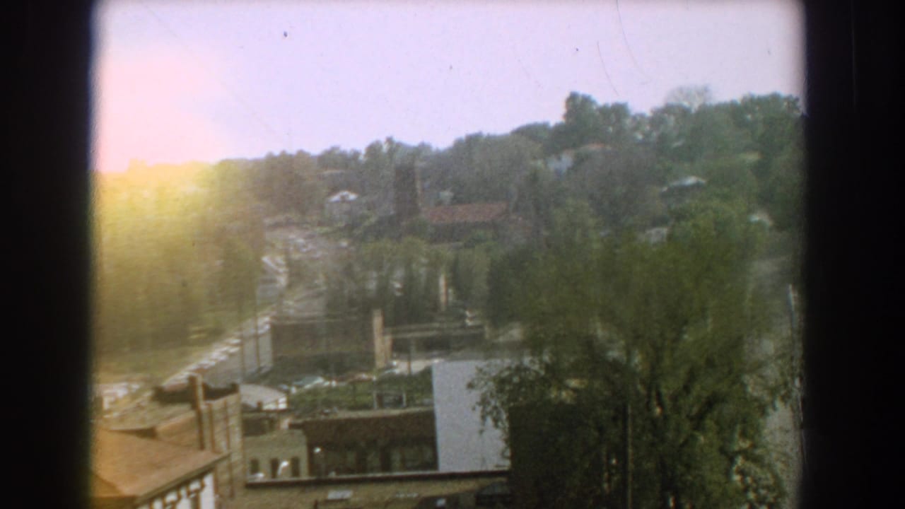 1959 Florida 8mm frame showing a sunlit elevated neighborhood view with trees, rooftops, and a pale shed-like structure.