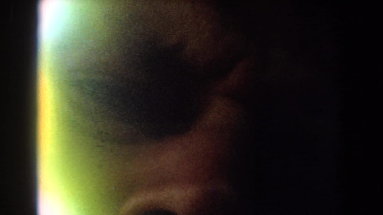 A dim, grainy 1959 8mm frame shows part of a person's face very close to the camera with a bright vertical flare at the left edge.