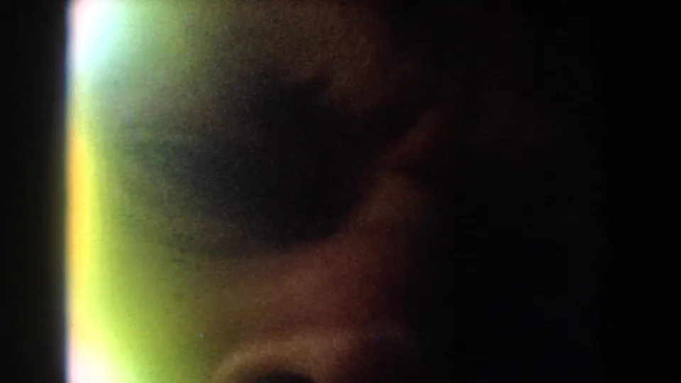 A dim, grainy 1959 8mm frame shows part of a person's face very close to the camera with a bright vertical flare at the left edge.
