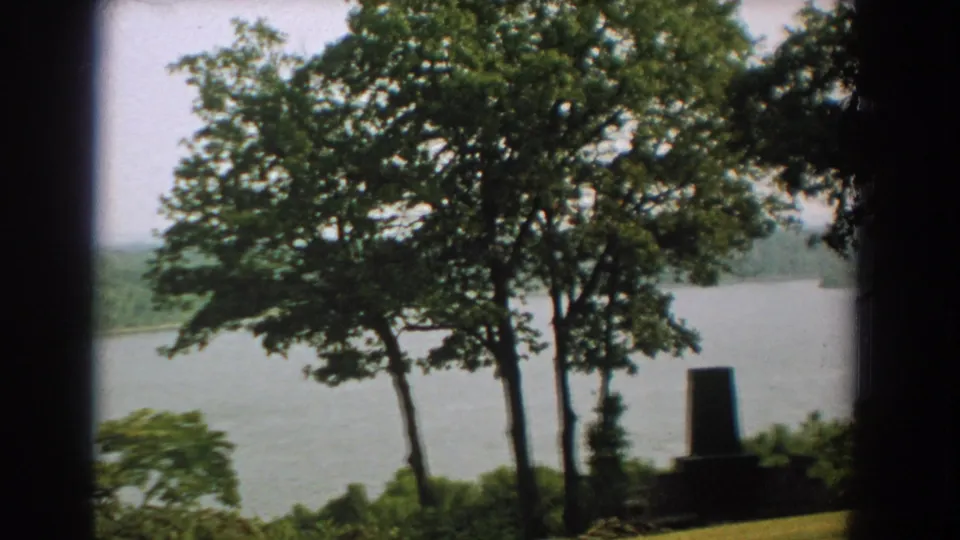 1959 Florida lakeside view with green trees, blue-green water, and a small dark monument-like form in the foreground.