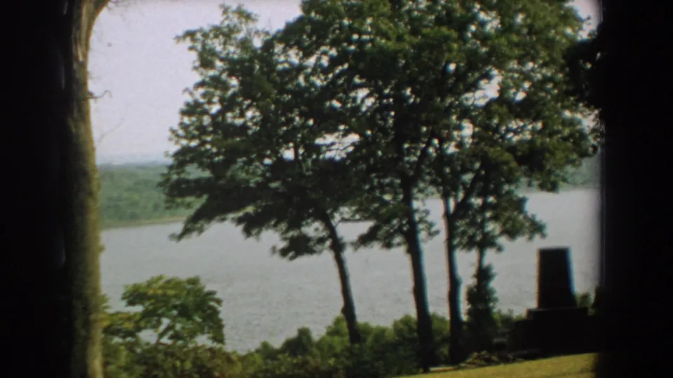 1959 Florida 8mm frame looking past trees and shrubs toward a calm lake and distant wooded shoreline.